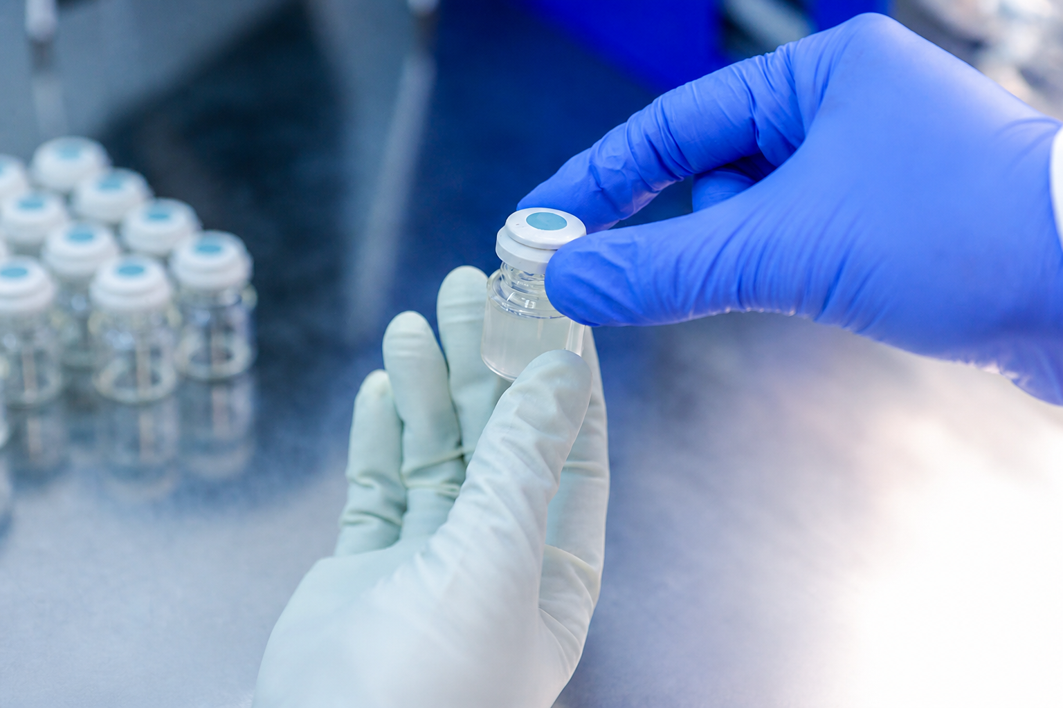Gloved hands inspecting a clear vial in a controlled laboratory
